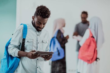 Üniversite yaşam tarzı yakışıklı Afrikalı bir öğrenci elinde tablet bilgisayarla üniversitenin karşısında durup gülümserken arka planda bir takım toplantısı yapıyor. Yüksek kalite