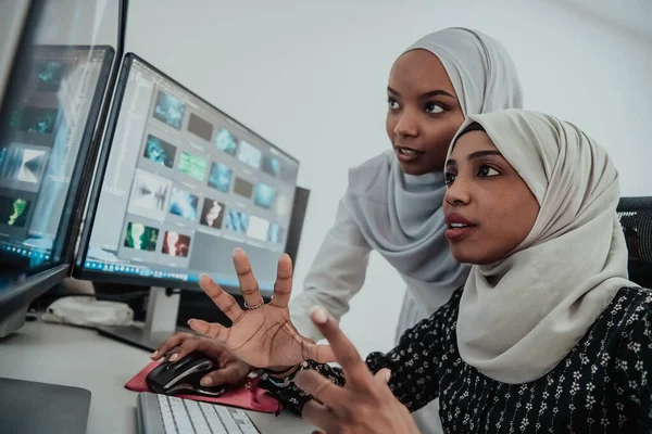 Amis au bureau deux jeunes femmes d'affaires afro-américaines musulmanes modernes portant une écharpe dans un bureau lumineux créatif avec un grand écran — Photo