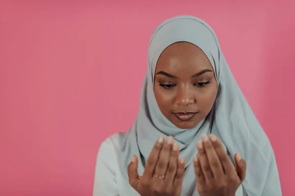 Femme musulmane africaine moderne fait la prière traditionnelle à Dieu, garde les mains dans le geste de prière, porte des vêtements blancs traditionnels, a une expression faciale sérieuse, isolé sur fond rose en plastique — Photo