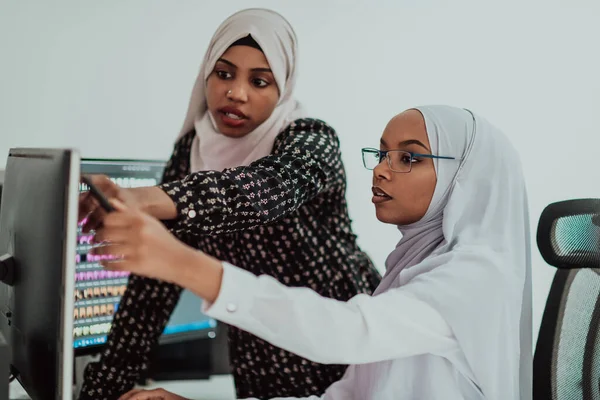 Amis au bureau deux jeunes femmes d'affaires afro-américaines musulmanes modernes portant une écharpe dans un bureau lumineux créatif avec un grand écran — Photo