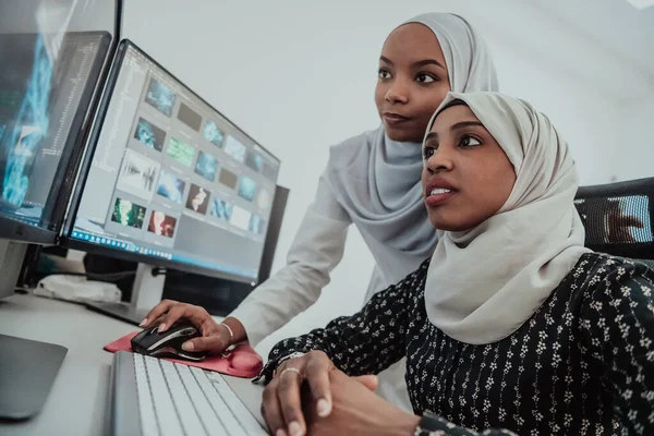 Amis au bureau deux jeunes femmes d'affaires afro-américaines musulmanes modernes portant une écharpe dans un bureau lumineux créatif avec un grand écran — Photo