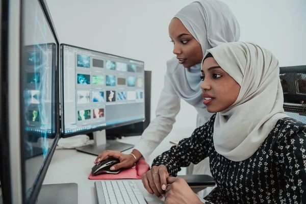 Amis au bureau deux jeunes femmes d'affaires afro-américaines musulmanes modernes portant une écharpe dans un bureau lumineux créatif avec un grand écran — Photo