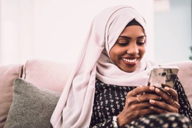 Afrikalı bir kadın evde koltukta otururken akıllı telefon kullanıyor..
