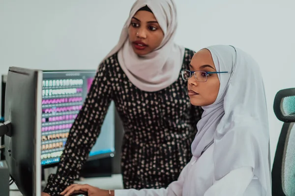 オフィスの友人2人の若いアフリカ系アメリカ人現代イスラム教徒のビジネス女性が大きな画面で創造的な明るいオフィスの職場でスカーフを着て — ストック写真