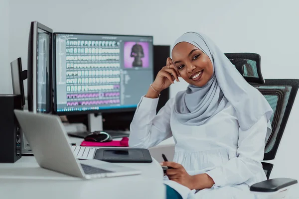 Ung afro-amerikansk modern Muselman affärskvinna bär en scarf i en kreativ ljus kontor arbetsplats med en stor skärm. — Stockfoto