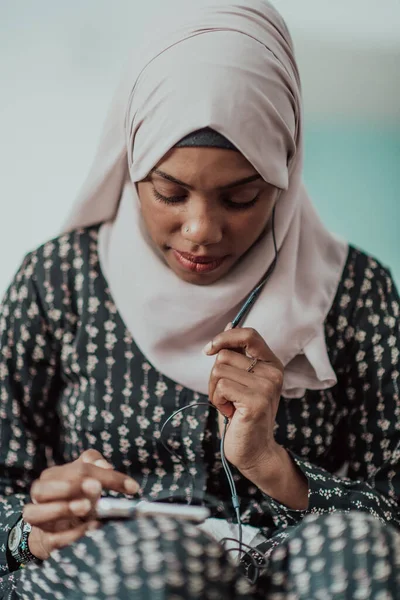 Afrikansk kvinna använder smartphone medan du sitter på soffan hemma bär hijab kläder. — Stockfoto