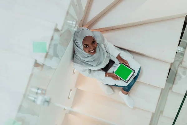 Ung afrikansk modern muslimsk kvinna använder surfplatta dator medan du sitter på trappan hemma bär hijab kläder ovanifrån — Stockfoto