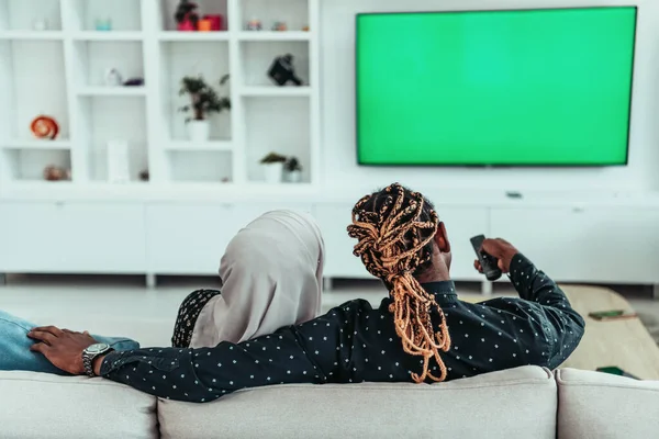 Afrikanisches Paar sitzt auf Sofa und sieht gemeinsam fern Chroma Green Screen Frau trägt islamische Hijab-Kleidung — Stockfoto