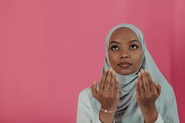 La moderna donna musulmana africana fa la preghiera tradizionale a Dio, tiene le mani nel gesto di preghiera, indossa abiti bianchi tradizionali, ha un'espressione facciale seria, isolata su uno sfondo rosa plastico — Foto Stock