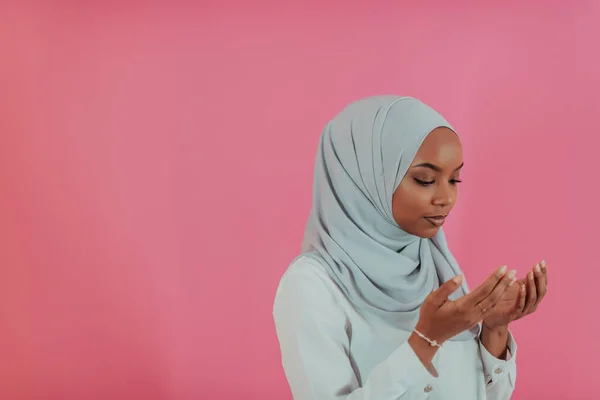 Femme musulmane africaine moderne fait la prière traditionnelle à Dieu, garde les mains dans le geste de prière, porte des vêtements blancs traditionnels, a une expression faciale sérieuse, isolé sur fond rose en plastique — Photo