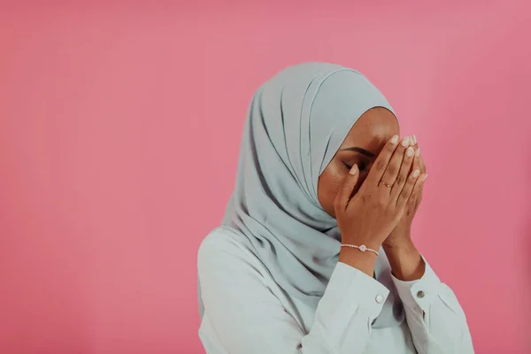 Modern afrikai muszlim nő teszi a hagyományos ima Istenhez, tartja a kezét imádkozó gesztus, visel hagyományos fehér ruhát, komoly arckifejezés, elszigetelt műanyag rózsaszín háttér — Stock Fotó