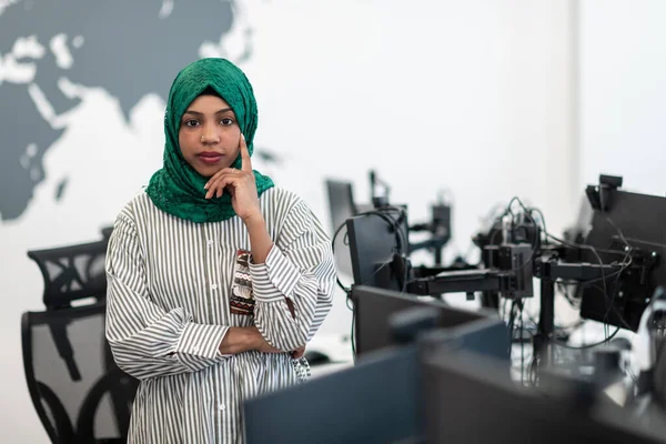 Retrato de desenvolvedor de software feminino preto muçulmano com hijab verde em pé no escritório de inicialização em plano aberto moderno. Foco seletivo — Fotografia de Stock