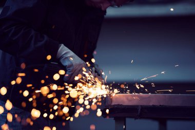 Heavy Industry Engineering Factory Interior with Industrial Worker Using Angle Grinder and Cutting a Metal Tube. Güvenlik Üniforması ve Sert Şapka Üretim Metal Yapıları Müteahhiti.