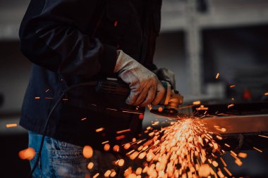 Heavy Industry Engineering Factory Interior with Industrial Worker Using Angle Grinder and Cutting a Metal Tube. Güvenlik Üniforması ve Sert Şapka Üretim Metal Yapıları Müteahhiti.