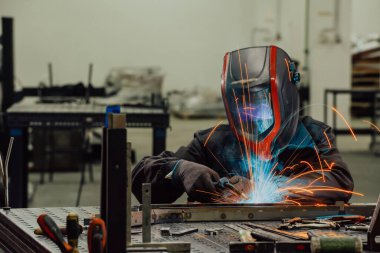 İçerideki fabrikada çalışan Profesyonel Ağır Sanayi Kaynakçısı, Kask Giyiyor ve Kaynak Yapmaya Başlıyor. Seçici Odaklanma