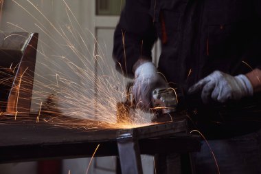 Heavy Industry Engineering Factory Interior with Industrial Worker Using Angle Grinder and Cutting a Metal Tube. Güvenlik Üniforması ve Sert Şapka Üretim Metal Yapıları Müteahhiti.