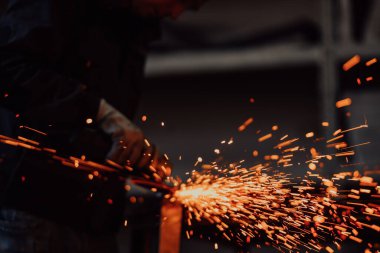 Heavy Industry Engineering Factory Interior with Industrial Worker Using Angle Grinder and Cutting a Metal Tube. Güvenlik Üniforması ve Sert Şapka Üretim Metal Yapıları Müteahhiti.