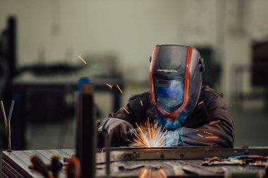 İçerideki fabrikada çalışan Profesyonel Ağır Sanayi Kaynakçısı, Kask Giyiyor ve Kaynak Yapmaya Başlıyor. Seçici Odaklanma