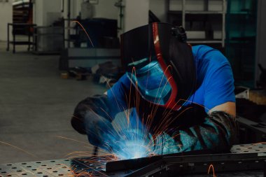 İçerideki fabrikada çalışan Profesyonel Ağır Sanayi Kaynakçısı, Kask Giyiyor ve Kaynak Yapmaya Başlıyor. Seçici Odaklanma
