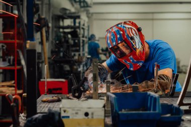 İçerideki fabrikada çalışan Profesyonel Ağır Sanayi Kaynakçısı, Kask Giyiyor ve Kaynak Yapmaya Başlıyor. Seçici Odaklanma