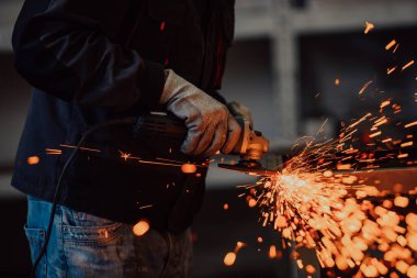 Heavy Industry Engineering Factory Interior with Industrial Worker Using Angle Grinder and Cutting a Metal Tube. Güvenlik Üniforması ve Sert Şapka Üretim Metal Yapıları Müteahhiti.