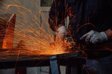 Heavy Industry Engineering Factory Interior with Industrial Worker Using Angle Grinder and Cutting a Metal Tube. Güvenlik Üniforması ve Sert Şapka Üretim Metal Yapıları Müteahhiti.
