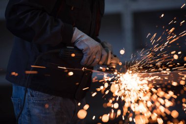 Heavy Industry Engineering Factory Interior with Industrial Worker Using Angle Grinder and Cutting a Metal Tube. Güvenlik Üniforması ve Sert Şapka Üretim Metal Yapıları Müteahhiti.