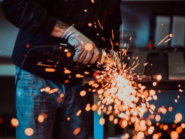 Heavy Industry Engineering Factory Interior with Industrial Worker Using Angle Grinder and Cutting a Metal Tube. Güvenlik Üniforması ve Sert Şapka Üretim Metal Yapıları Müteahhiti.
