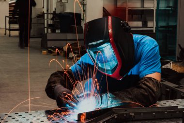 İçerideki fabrikada çalışan Profesyonel Ağır Sanayi Kaynakçısı, Kask Giyiyor ve Kaynak Yapmaya Başlıyor. Seçici Odaklanma