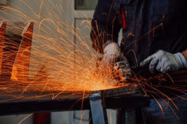 Heavy Industry Engineering Factory Interior with Industrial Worker Using Angle Grinder and Cutting a Metal Tube. Güvenlik Üniforması ve Sert Şapka Üretim Metal Yapıları Müteahhiti.