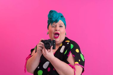 Artı, komik duygusal yüz ifadesi olan, pembe arka planda izole edilmiş kot elbiseli klasik kameralı, gülümseyen kadın, tatilde gezgin, yaz modası tarzı, heyecanlı turist..