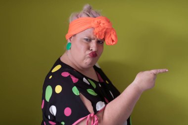 Artı, modaya uygun makyajlı seksi model kadın, stüdyoda yeşil arka planda poz veren siyah kısa elbiseli şık sarışın..