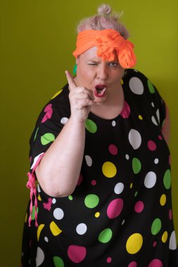 Artı, modaya uygun makyajlı seksi model kadın, stüdyoda yeşil arka planda poz veren siyah kısa elbiseli şık sarışın..