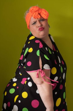 Artı, modaya uygun makyajlı seksi model kadın, stüdyoda yeşil arka planda poz veren siyah kısa elbiseli şık sarışın..