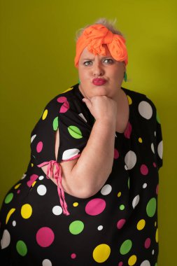 Artı, modaya uygun makyajlı seksi model kadın, stüdyoda yeşil arka planda poz veren siyah kısa elbiseli şık sarışın..