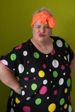 Artı, modaya uygun makyajlı seksi model kadın, stüdyoda yeşil arka planda poz veren siyah kısa elbiseli şık sarışın..