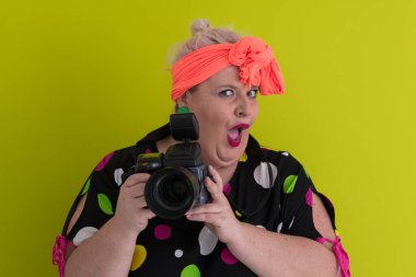 Artı, komik duygusal yüz ifadesi olan, yeşil arka planda izole edilmiş klasik kameralı, gülümseyen bir kadın, tatilde gezgin, yaz modası tarzı, heyecanlı bir turist..