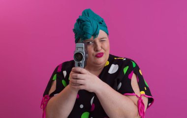 Artı, komik duygusal yüz ifadesi olan, pembe arka planda izole edilmiş eski moda kameralı, yaz modası tarzında gezgin, heyecanlı turist tipli, gülen bir kadın..