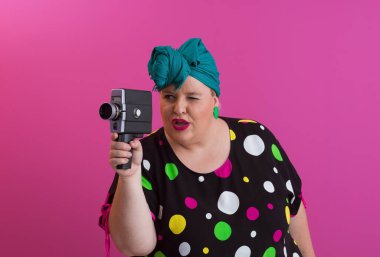 Artı, komik duygusal yüz ifadesi olan, pembe arka planda izole edilmiş eski moda kameralı, yaz modası tarzında gezgin, heyecanlı turist tipli, gülen bir kadın..