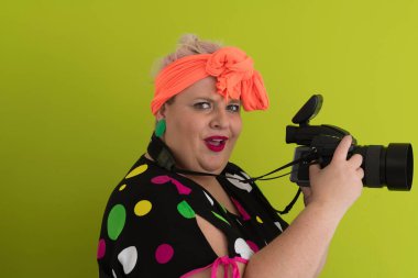 Artı, komik duygusal yüz ifadesi olan, yeşil arka planda izole edilmiş klasik kameralı, gülümseyen bir kadın, tatilde gezgin, yaz modası tarzı, heyecanlı bir turist..