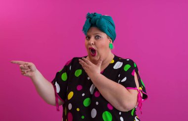 Artı, modaya uygun makyajlı seksi model kadın, stüdyoda pembe arka planda poz veren siyah kısa elbiseli şık sarışın..