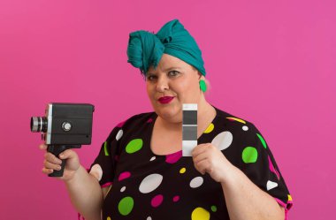 Artı, komik duygusal yüz ifadesi olan, pembe arka planda izole edilmiş eski moda kameralı, yaz modası tarzında gezgin, heyecanlı turist tipli, gülen bir kadın..