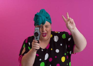 Artı, komik duygusal yüz ifadesi olan, pembe arka planda izole edilmiş eski moda kameralı, yaz modası tarzında gezgin, heyecanlı turist tipli, gülen bir kadın..