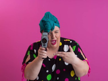 Artı, komik duygusal yüz ifadesi olan, pembe arka planda izole edilmiş eski moda kameralı, yaz modası tarzında gezgin, heyecanlı turist tipli, gülen bir kadın..