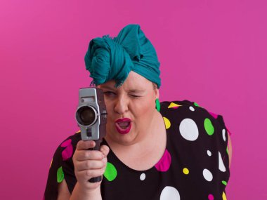 Artı, komik duygusal yüz ifadesi olan, pembe arka planda izole edilmiş eski moda kameralı, yaz modası tarzında gezgin, heyecanlı turist tipli, gülen bir kadın..