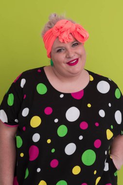 Artı, modaya uygun makyajlı seksi model kadın, stüdyoda yeşil arka planda poz veren siyah kısa elbiseli şık sarışın..