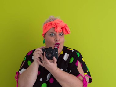 Artı, komik duygusal yüz ifadesi olan, yeşil arka planda izole edilmiş klasik kameralı, gülümseyen bir kadın, tatilde gezgin, yaz modası tarzı, heyecanlı bir turist..