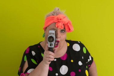 Artı, komik duygusal yüz ifadesi olan, yeşil arka planda izole edilmiş klasik kameralı, gülümseyen bir kadın, tatilde gezgin, yaz modası tarzı, heyecanlı bir turist..