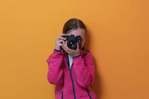 노란 배경에 고립된 어린 소녀 사진사는 고전풍의 카메라로 사진을 찍으면서 웃고 있었다. — 스톡 사진
