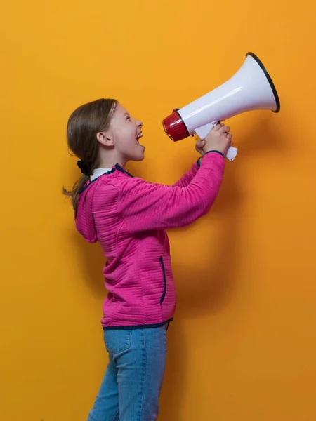 Funny little kid girl Screaming in megaphone over the yellow background in studio. People sincere emotions lifestyle concept. — Stock fotografie